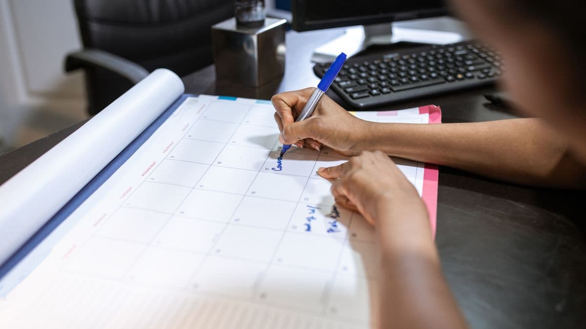 Una mano escribe en un calendario de escritorio