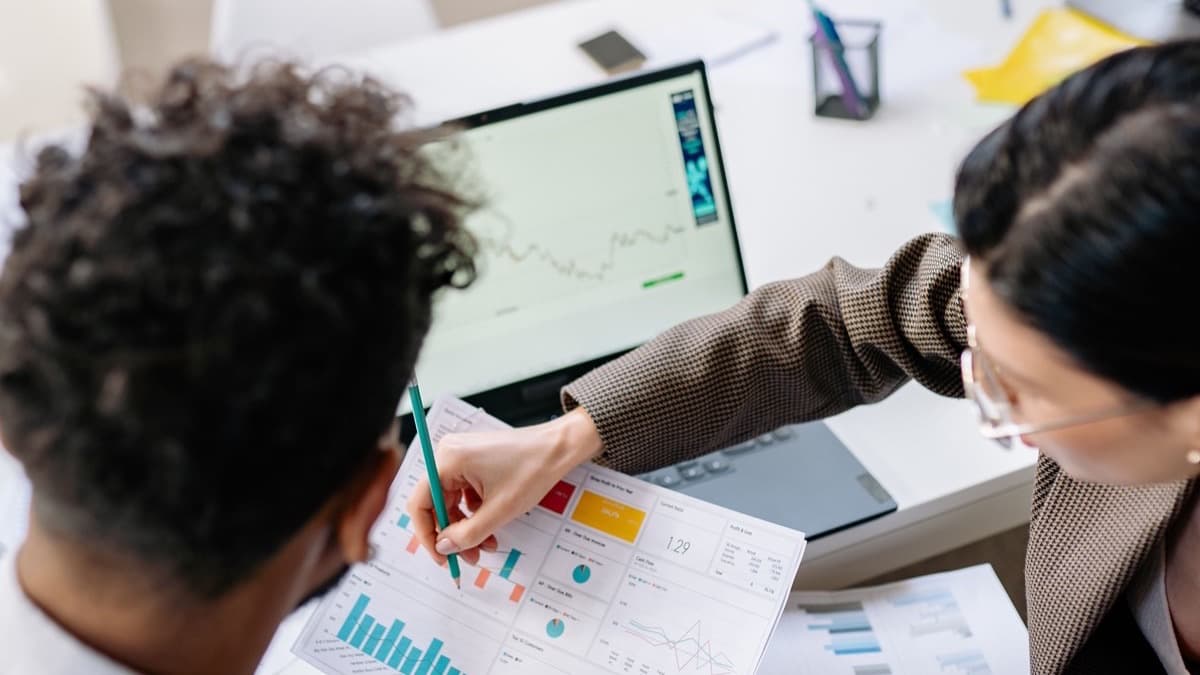Dos personas revisan gráficas impresas junto a una laptop